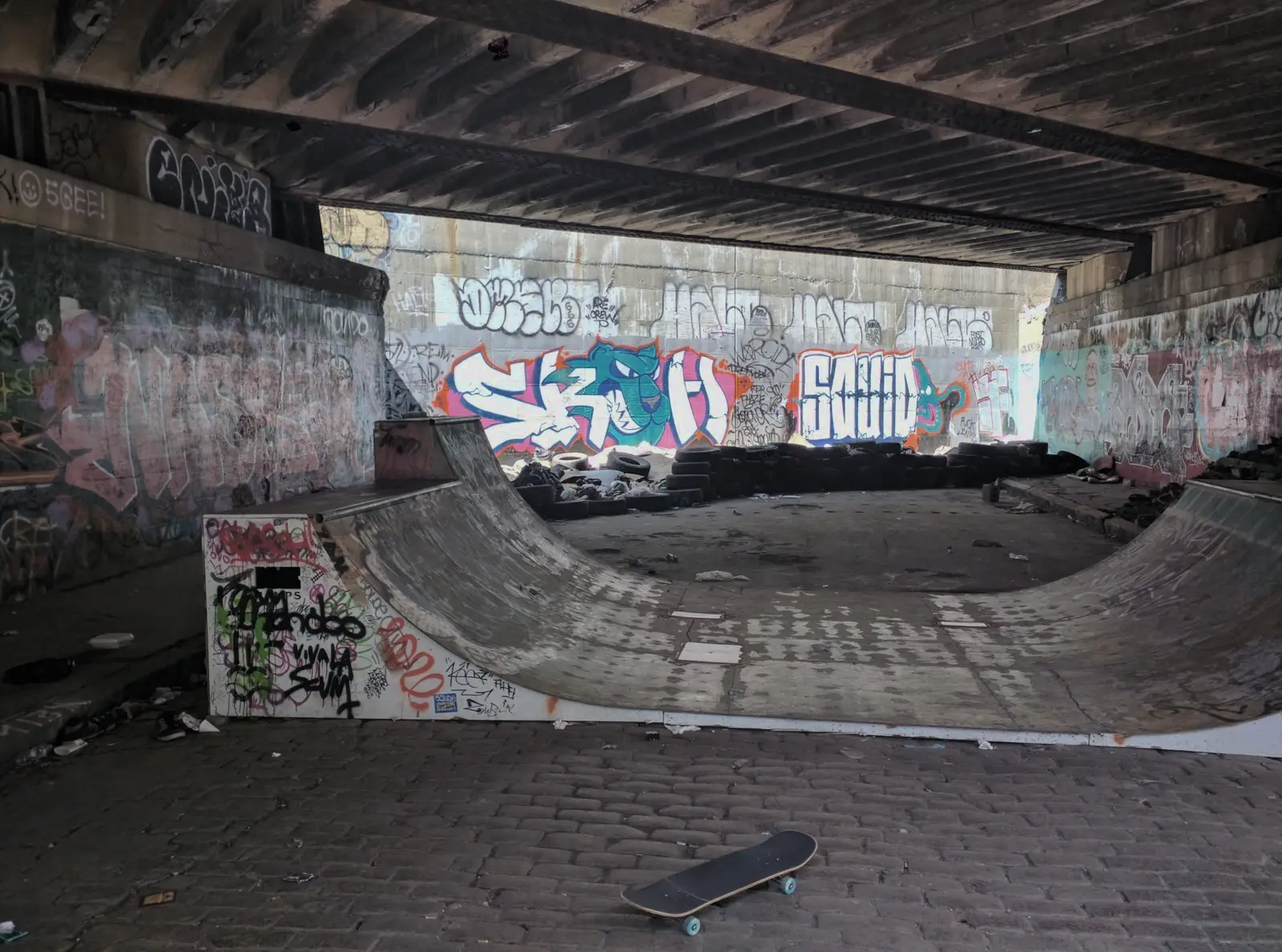 Skateboard under a bridge at a graffiti-covered DIY spot